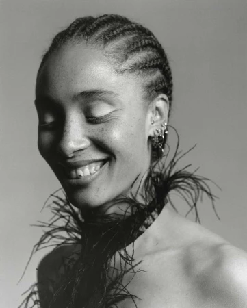 Monochrome portrait of a Black woman with braided hair, eyes closed, and a cheerful smile, accessorized with a black feather boa.