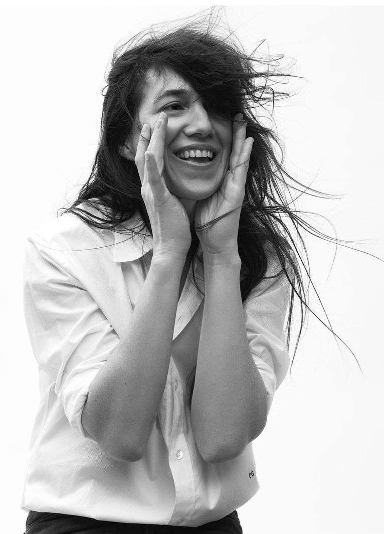 Black and white portrait of a smiling woman with windblown hair wearing a white button-down shirt holding her face