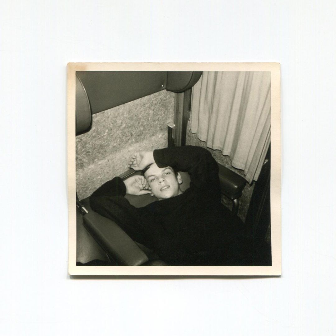Monochrome portrait of a young adult lying down with hands near the head and looking at the camera in an indoor environment.