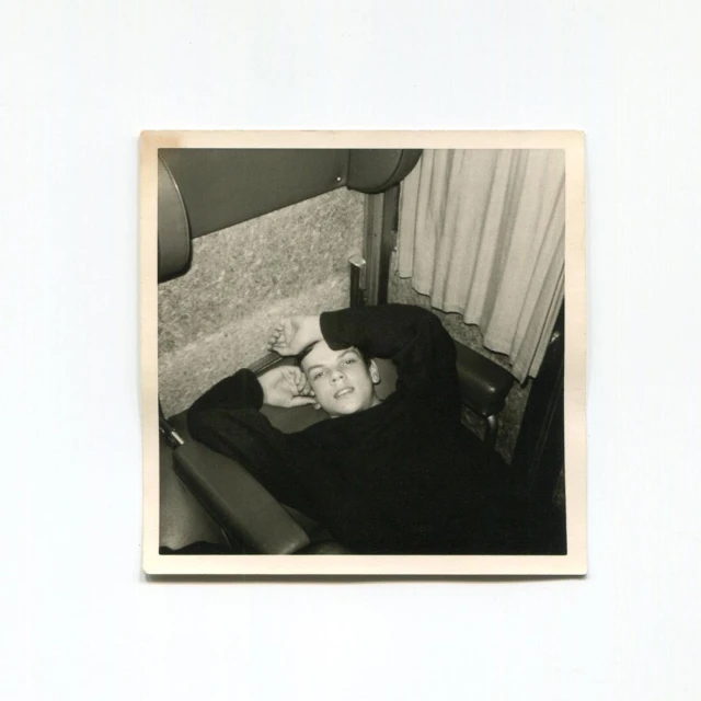 Monochrome portrait of a young adult lying down with hands near the head and looking at the camera in an indoor environment.