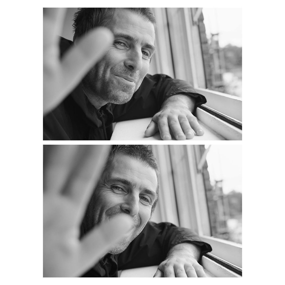 Monochrome portrait of a smiling adult man waving from a window, head and shoulders shot, soft window light, casual dark shirt.