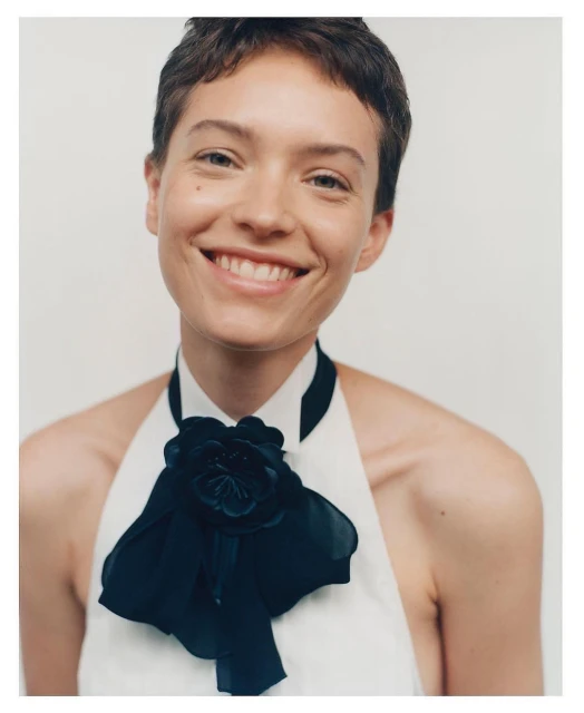 Close-up portrait of an adult woman smiling, wearing a white top adorned with a large black bow with a flower detail.