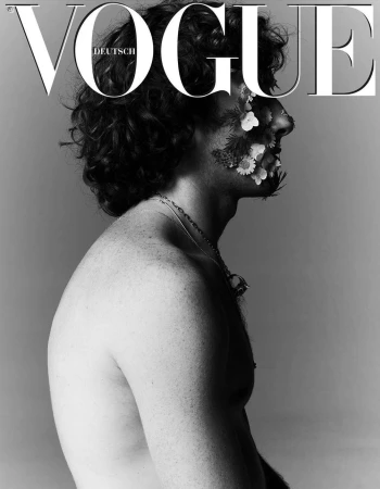 Black and white portrait of a shirtless man in profile with white flowers arranged across his cheek, photographed by Stefan Heinrichs.