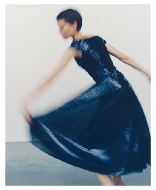 Fashion shot of a woman with short hair wearing a dark dress in motion against a white background, creating a blurred effect.