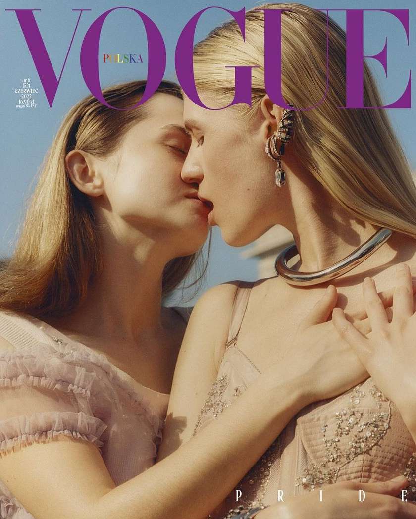 Vogue Polska cover featuring two fair-skinned adult females embracing and kissing, blonde hair, light pink dresses, jewelry, and a blue sky background.