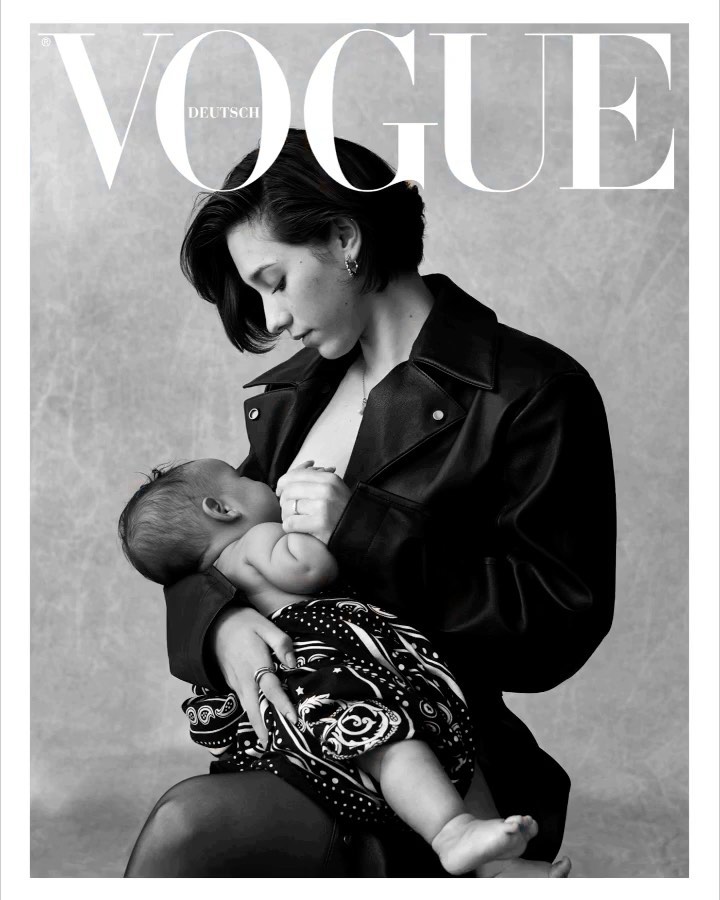 Black and white portrait of an adult female wearing a jacket, holding and breastfeeding a baby in front of a textured background.