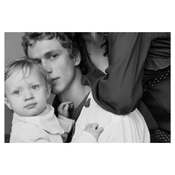 Black and white portrait of a man holding a young child with another person embracing from behind, photographed by Stefan Heinrichs.