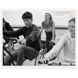 Group of young people riding bicycles along a coastal path in a black and white photograph by Stefan Heinrichs
