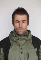 Liam Gallagher with eyes closed wearing an olive green hooded jacket against a white background