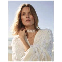 Portrait of a woman wearing a white fringe cardigan outdoors against a blurred beach background by Stefan Heinrichs