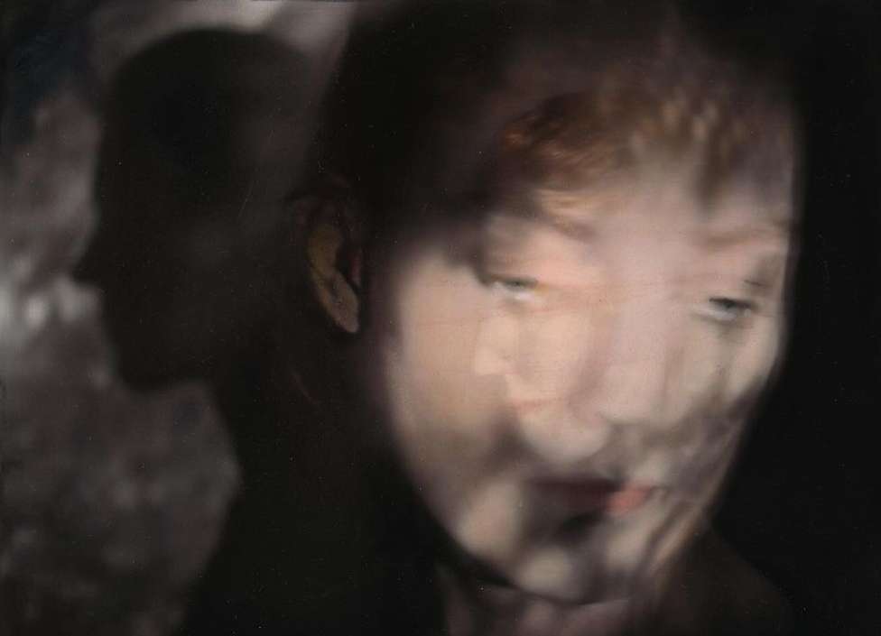 Abstract portrait of a person's face with red hair, softly focused, alongside a darker silhouetted profile in a shadowy background.