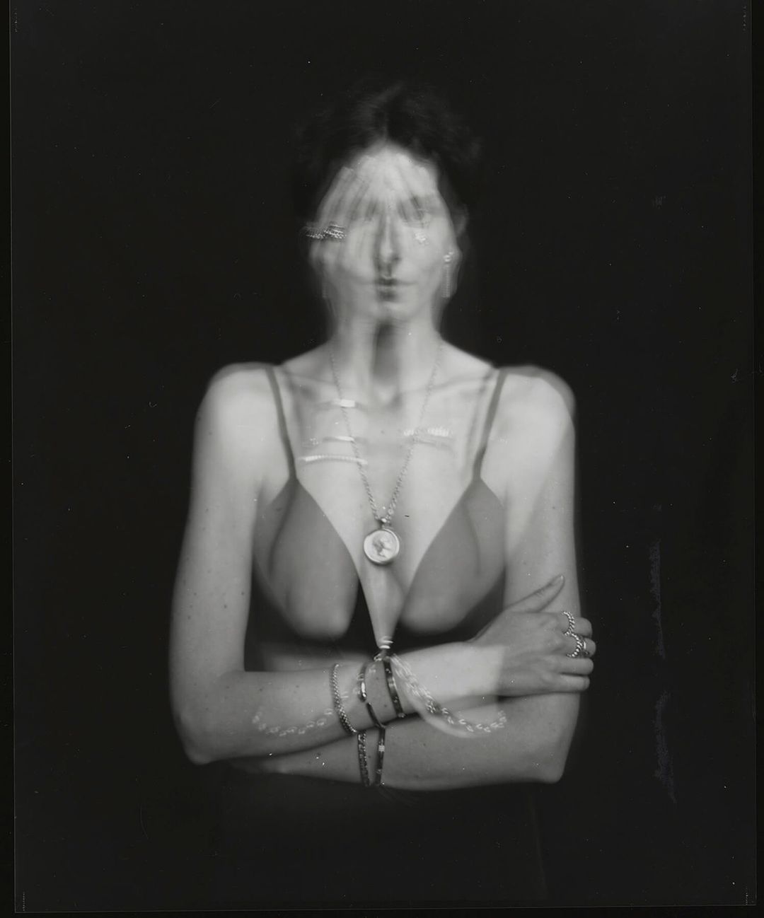 Monochrome portrait of a woman with blurred motion, wearing a camisole top and multiple bracelets, against a solid black background.