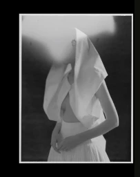 Black and white portrait of a woman wearing a white sculptural garment and head covering with blurred features