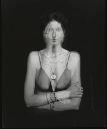 Portrait of a woman with blurred multiple exposure hand gestures wearing a pendant necklace against a dark background