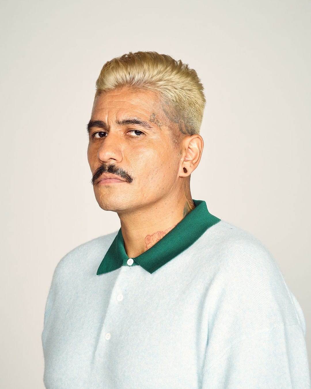 Portrait of adult man with blonde hair and mustache wearing polo shirt against neutral background, studio shot.