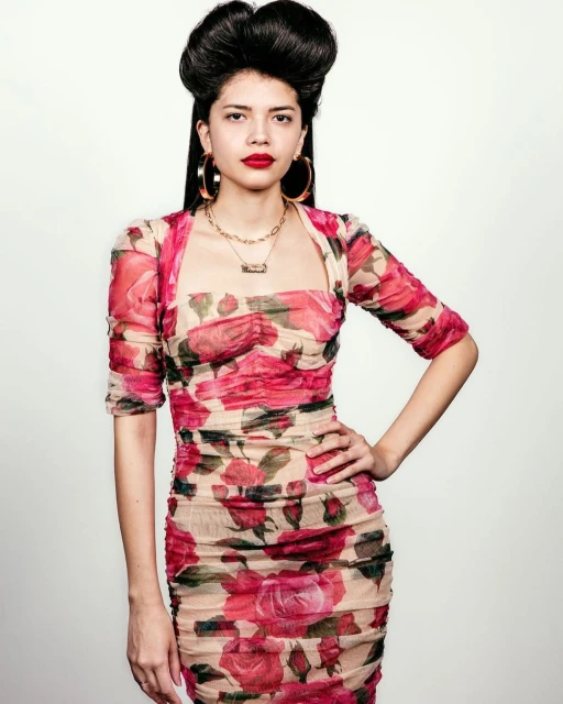 Portrait of a stylish young woman with a high hairstyle and floral dress, posing in front of a neutral backdrop with studio lighting.