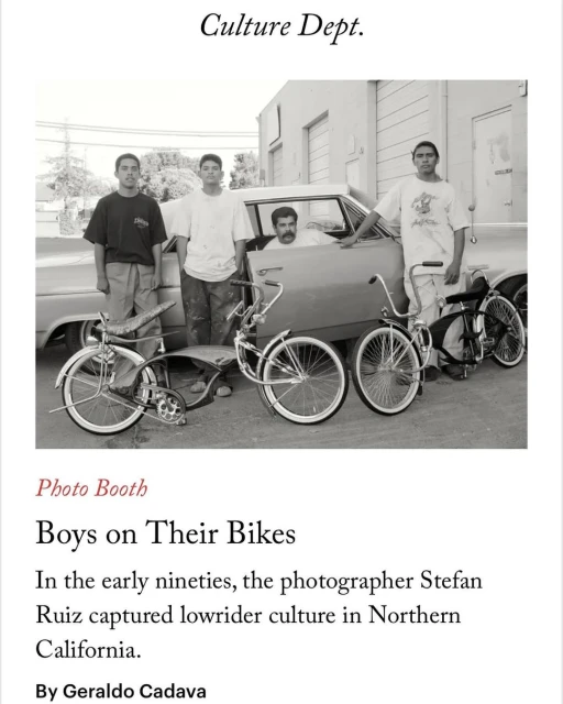 Four young men pose with lowrider bicycles and a vintage car in a black and white outdoor shot, showcasing lowrider culture.