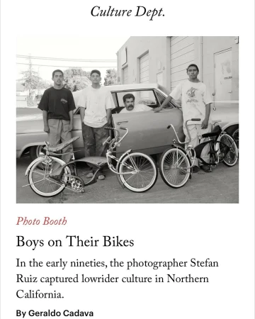 Four young men pose with lowrider bicycles and a vintage car in a black and white outdoor shot, showcasing lowrider culture.