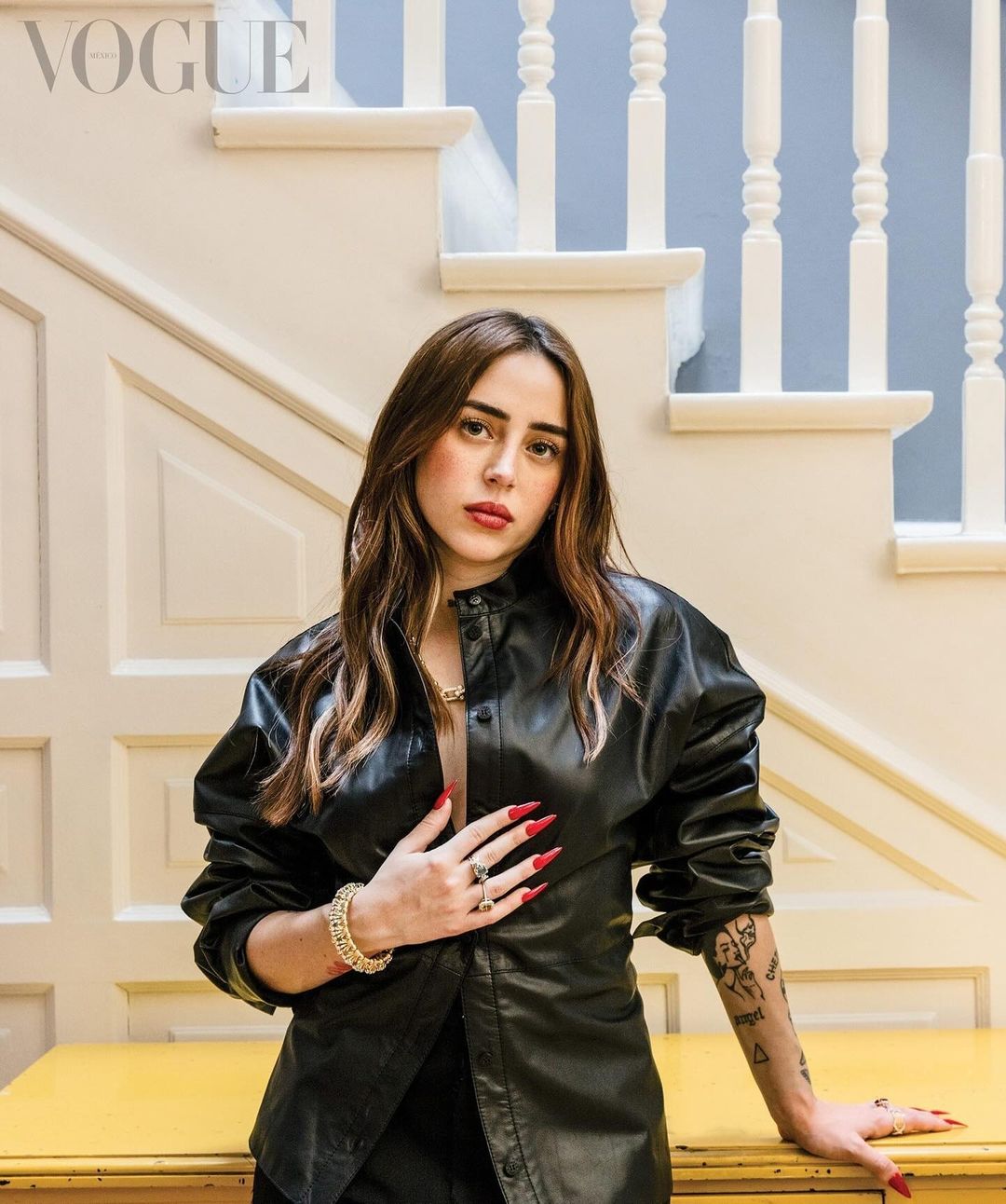 Portrait of a woman wearing a black leather shirt standing in front of a white staircase and yellow furniture