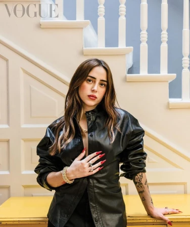Portrait of a woman wearing a black leather shirt standing in front of a white staircase and yellow furniture