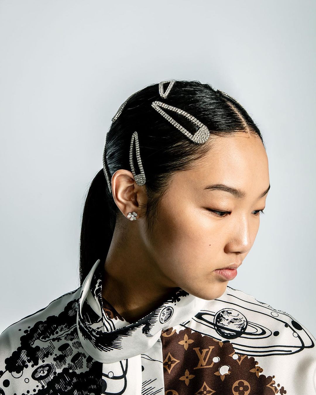 Portrait of an Asian woman with hair clips, wearing a patterned blouse, in a photo studio with soft lighting and a neutral background.