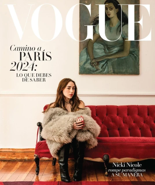 Vogue cover featuring a woman with long brown hair, wearing a fur coat and sitting on a red velvet couch against a white wall.