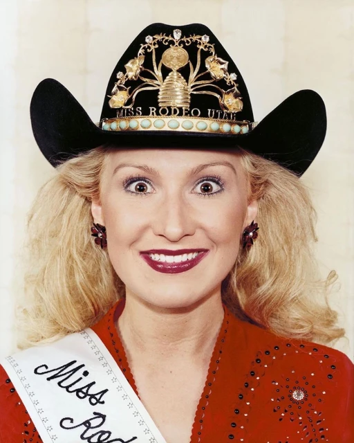 Portrait of a smiling woman wearing a black cowboy hat adorned with jewels and a sash, in a red beaded western style shirt.