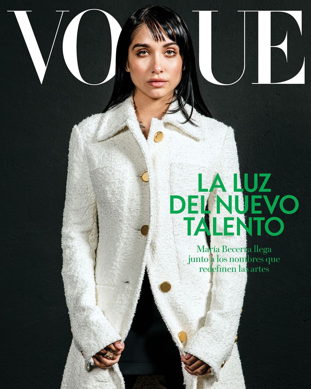 Portrait of María Becerra wearing a white textured coat against a dark textured background for a Vogue magazine cover.