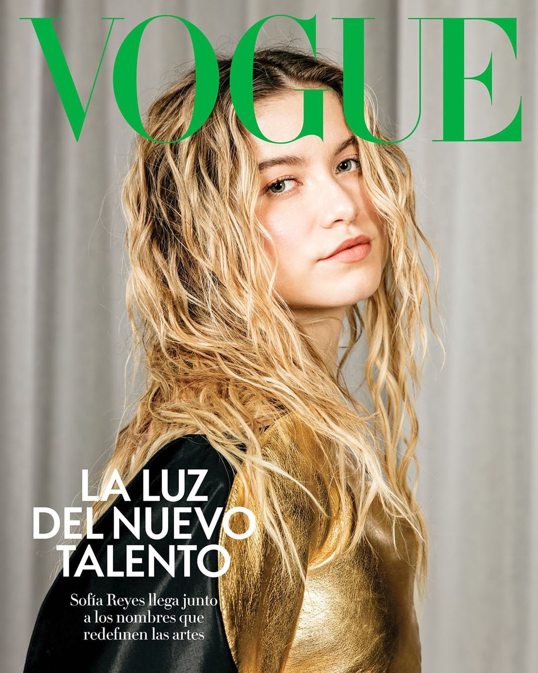 Vogue magazine cover featuring a young adult female with wavy blonde hair, wearing a gold top, posing in front of a neutral background.