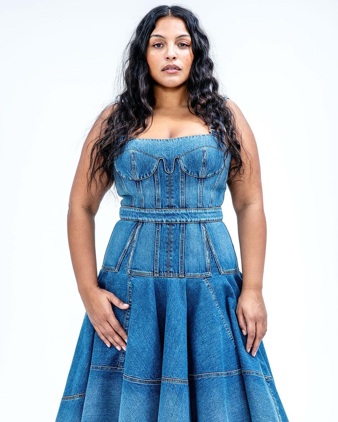 Portrait of a woman wearing a denim dress in a studio environment with a plain white background, showcasing fashion and style.