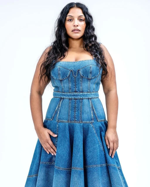 Portrait of a woman wearing a denim dress in a studio environment with a plain white background, showcasing fashion and style.