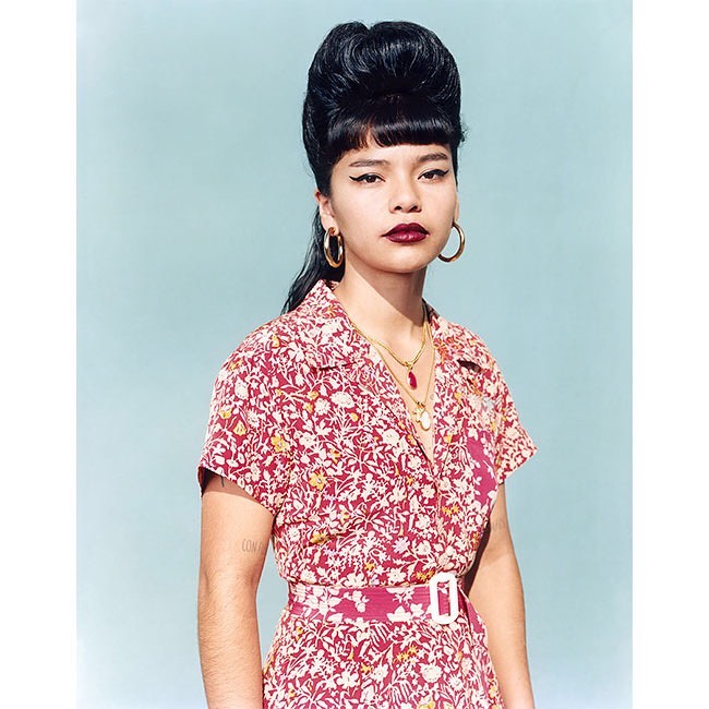 Portrait of a stylish Asian woman with an elegant updo, hoop earrings, and a red floral shirt dress against a light blue backdrop.