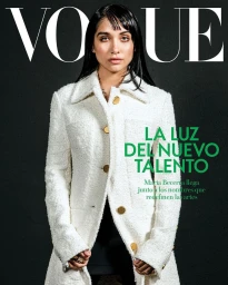 Magazine cover portrait of a woman with dark hair wearing a white textured coat with gold buttons against a dark background