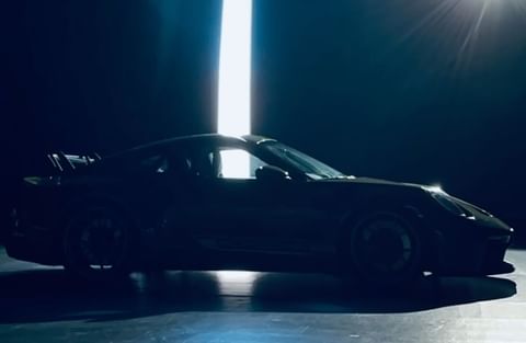 Silhouette of a dark-colored Porsche sports car in a studio with bright vertical light in the background, low angle, automotive content.