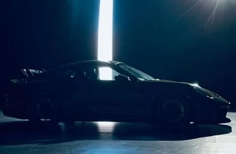 Silhouette of a dark-colored Porsche sports car in a studio with bright vertical light in the background, low angle, automotive content.