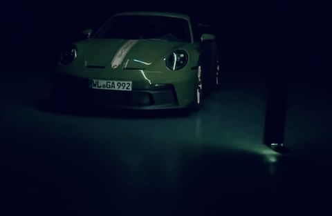 A green Porsche 911 GT3 car is parked indoors with dim lighting, highlighting its sleek design and athletic stance.