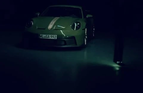 A green Porsche 911 GT3 car is parked indoors with dim lighting, highlighting its sleek design and athletic stance.