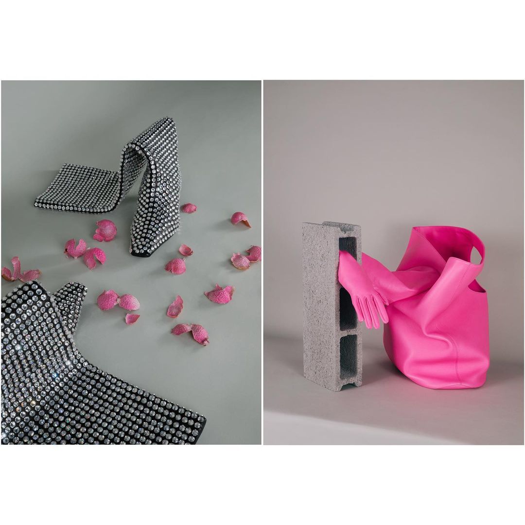 Fashion still life featuring a sparkling, bejeweled high heel shoe and a rubber glove placed between a cinder block and a pink handbag.