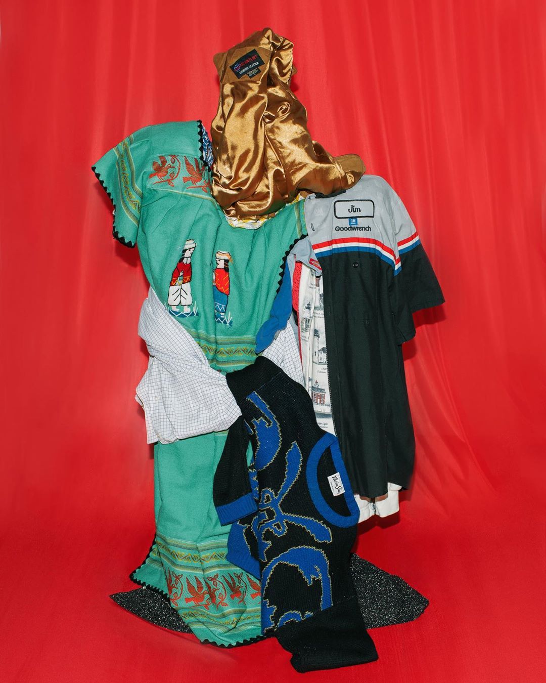 Display of assorted clothing items, including dresses, shirts, and pants, arranged on a red surface in a vertical composition.