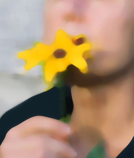 Close-up of a person holding a yellow flower to their face with dark brown centers against a soft, blurred grey background.