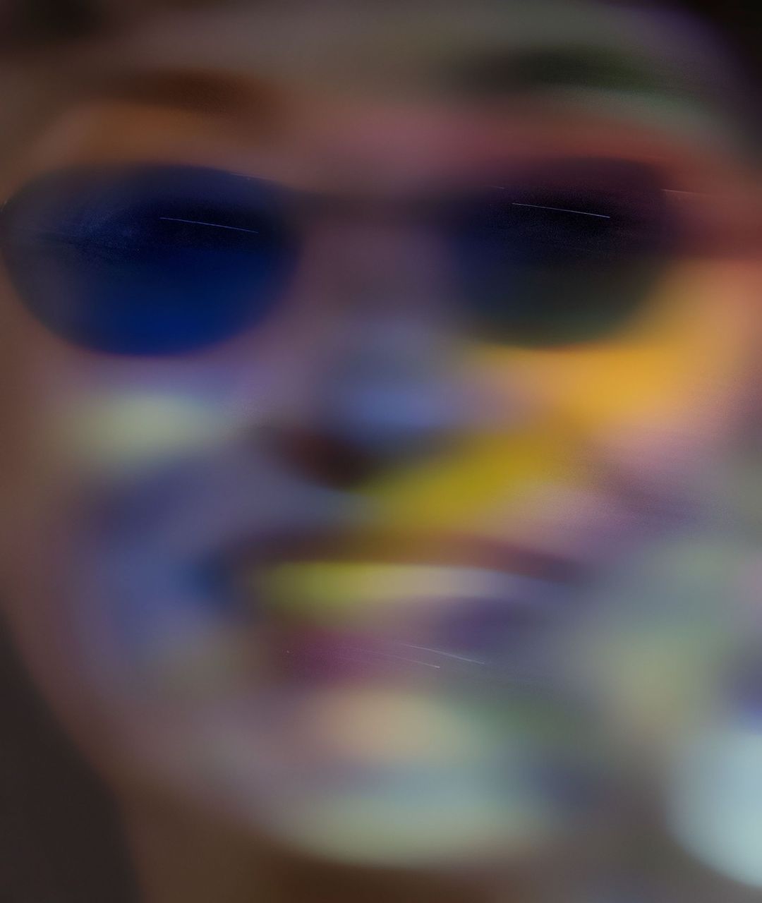 Abstract portrait of a person with sunglasses and colorful lighting effects, creating a dreamy and artistic blurred aesthetic.