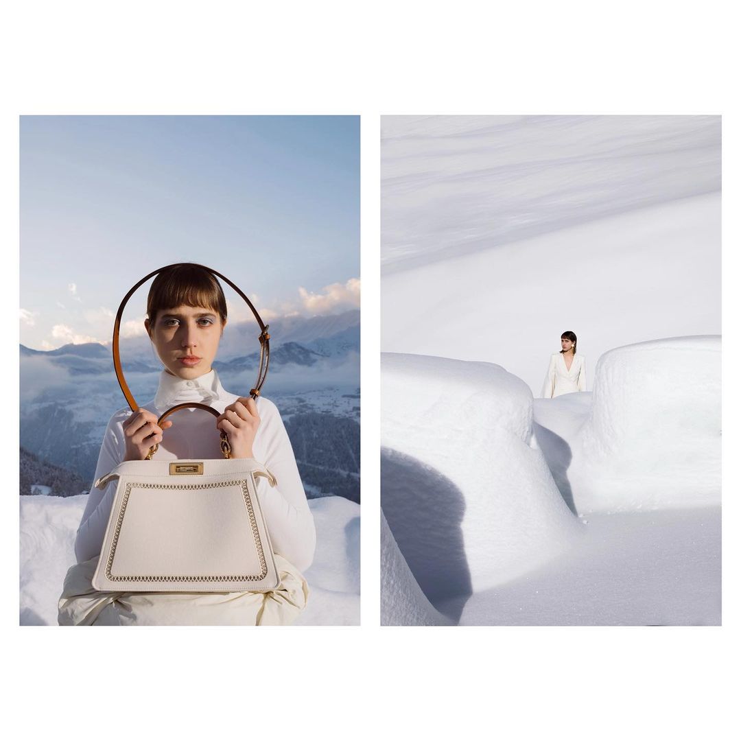 Fashion shot in the snow-covered mountains featuring a woman in a white outfit holding a white Fendi handbag with a brown handle.