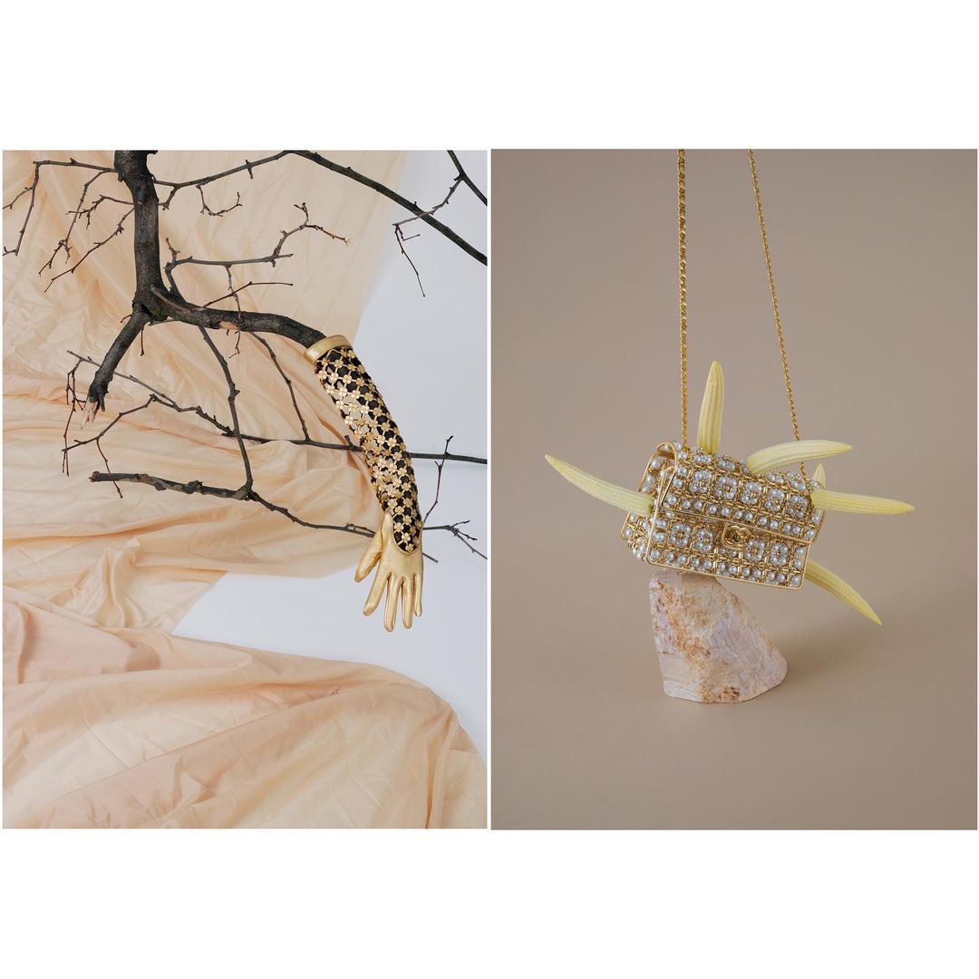 Still life fashion shot: a crystal-embellished handbag on a rock, contrasted with a gold-painted, patterned glove on a bare branch.