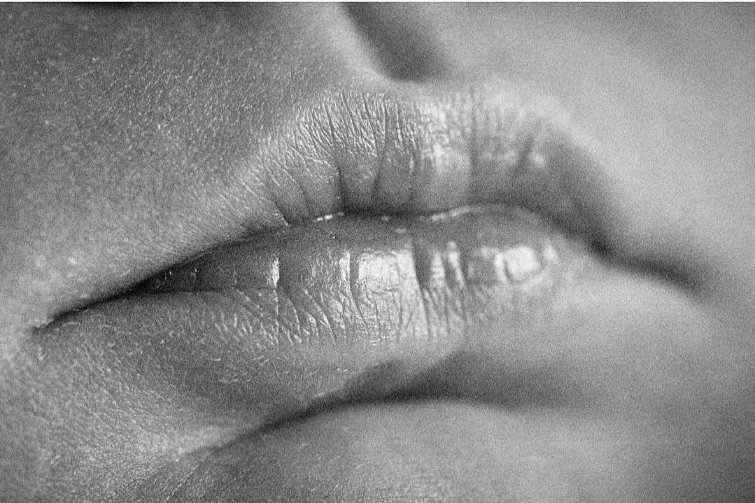 Close-up of human lips in a black and white photograph, focusing on the texture of the skin and lip lines under natural lighting.