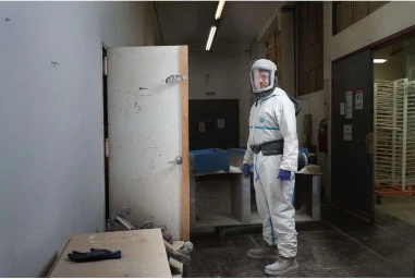 Man wearing a full white hazmat suit with a clear helmet and blue gloves standing inside an industrial interior