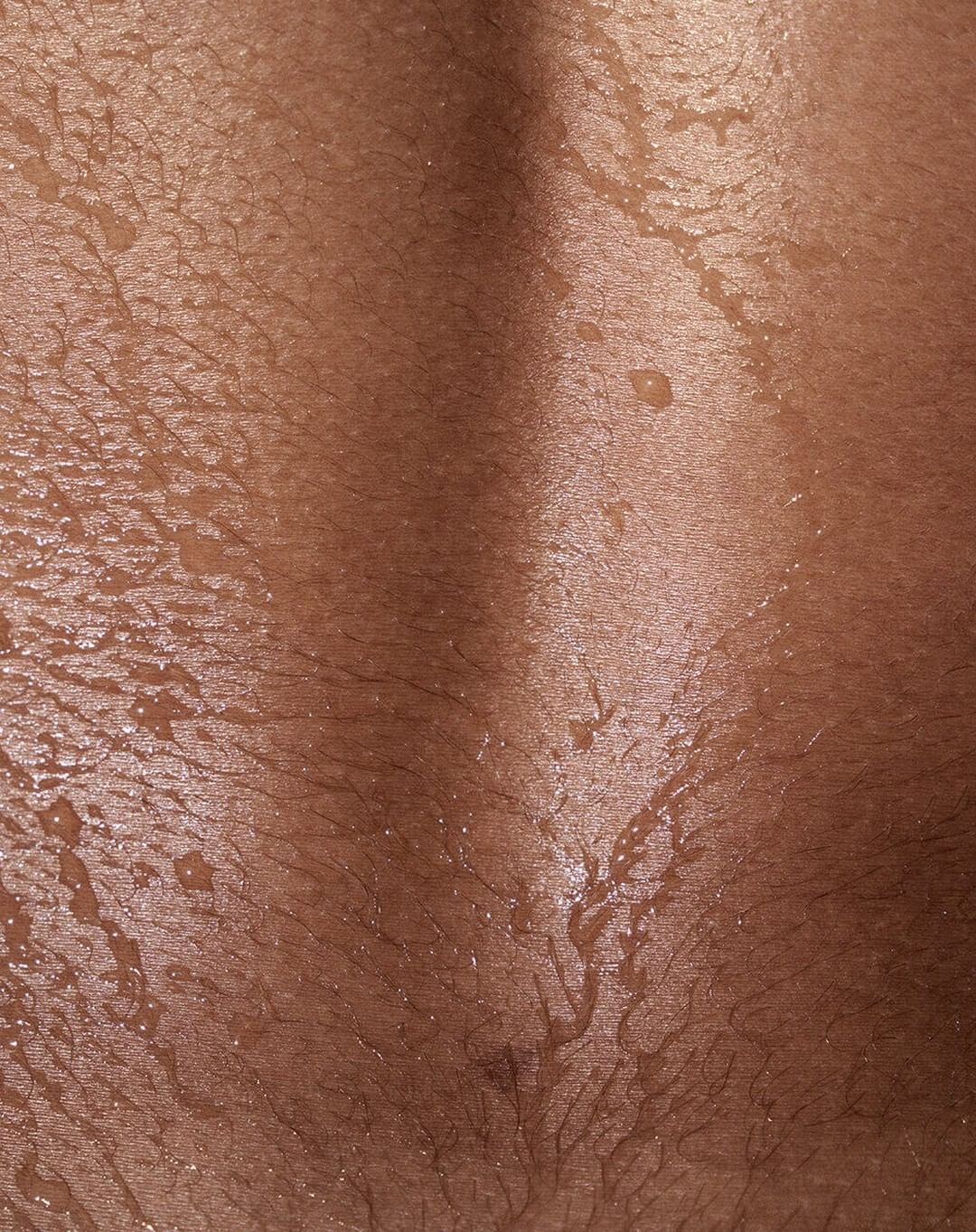 Close-up on tan skin showing sweat or water droplets, with hair visible. Shallow depth of field and warm lighting.