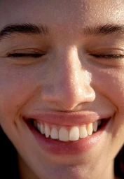 Close-up macro portrait of a person smiling with eyes closed in warm natural sunlight highlighting skin texture