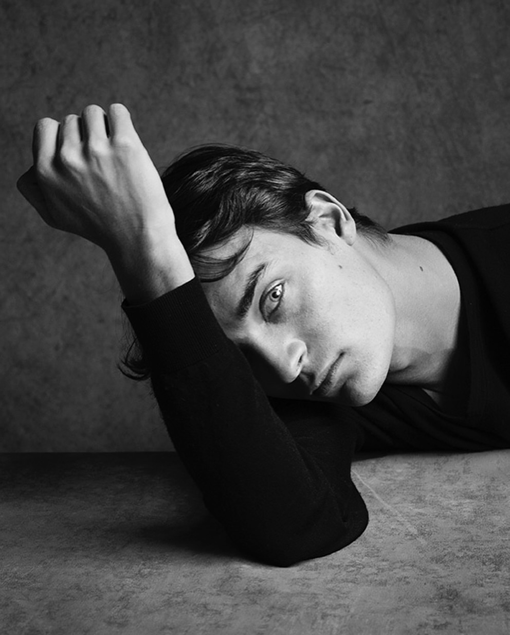 Portrait of a man resting his head on his arm against a dark textured background by Stephan Vanfleteren