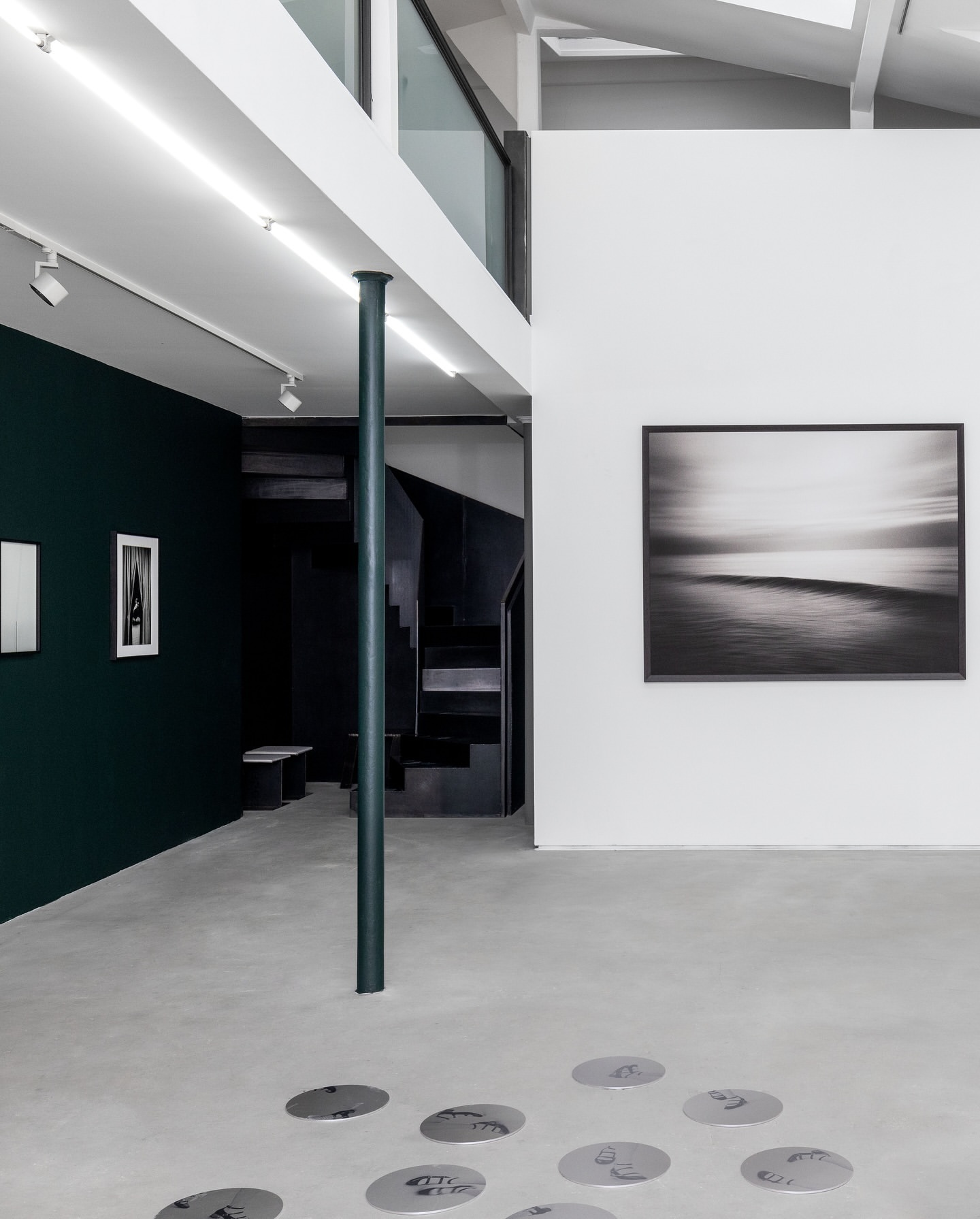 Minimalist interior of a modern art gallery with concrete floors, white walls, dark green accent wall, and framed black and white photography.