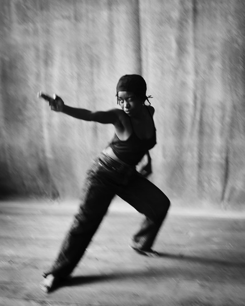 Black and white action shot of a young adult wearing a cap, tank top, and jeans with a blurred background, creating a sense of movement.